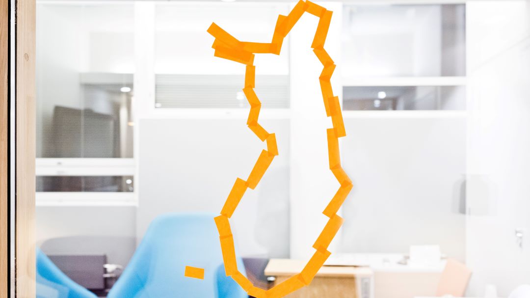Keltaisista lapuista tehty Suomen kartan ääriviivat. Taustalla kalustettu huone.