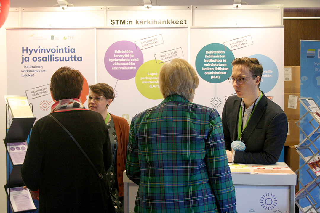 Kärkihankkeiden asiantuntijat keskustelemassa messuvieraiden kanssa. Taustalla kärkihankkeiden esittelykankaat.