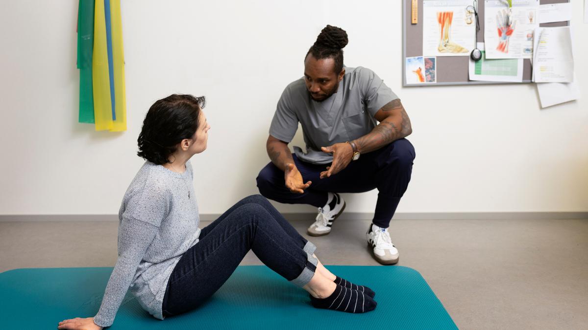 Kuvassa on asiakas jumppamatolla ja fysioterapeutti opastaa häntä.