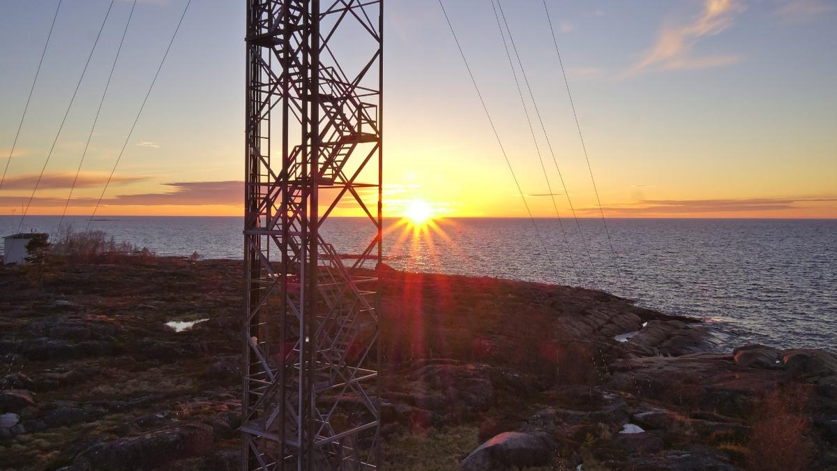 Etualalla masto, taustalla merta ja auringonlasku