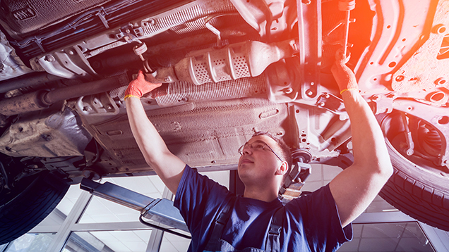A mechanic investigates a bottom of a car in service station.
