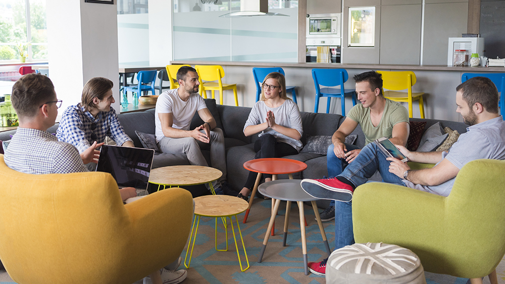 Kuvassa on kuusi ihmistä kokouksessa istumassa vapaamuotoisesti puolikaaressa. He suunnittelevat yhdessä työtään.